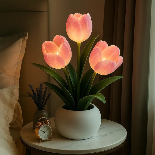 Lumiere Blossom LED decorative lamp featuring three glowing pink tulip lights in a white pot, placed on a round bedside table next to an alarm clock and a small vase.