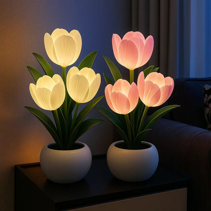 Two Lumiere Blossom LED decorative tulip lamps, one glowing warm white and the other pink, both in elegant white pots, displayed on a dark table in a cozy, dimly lit room.